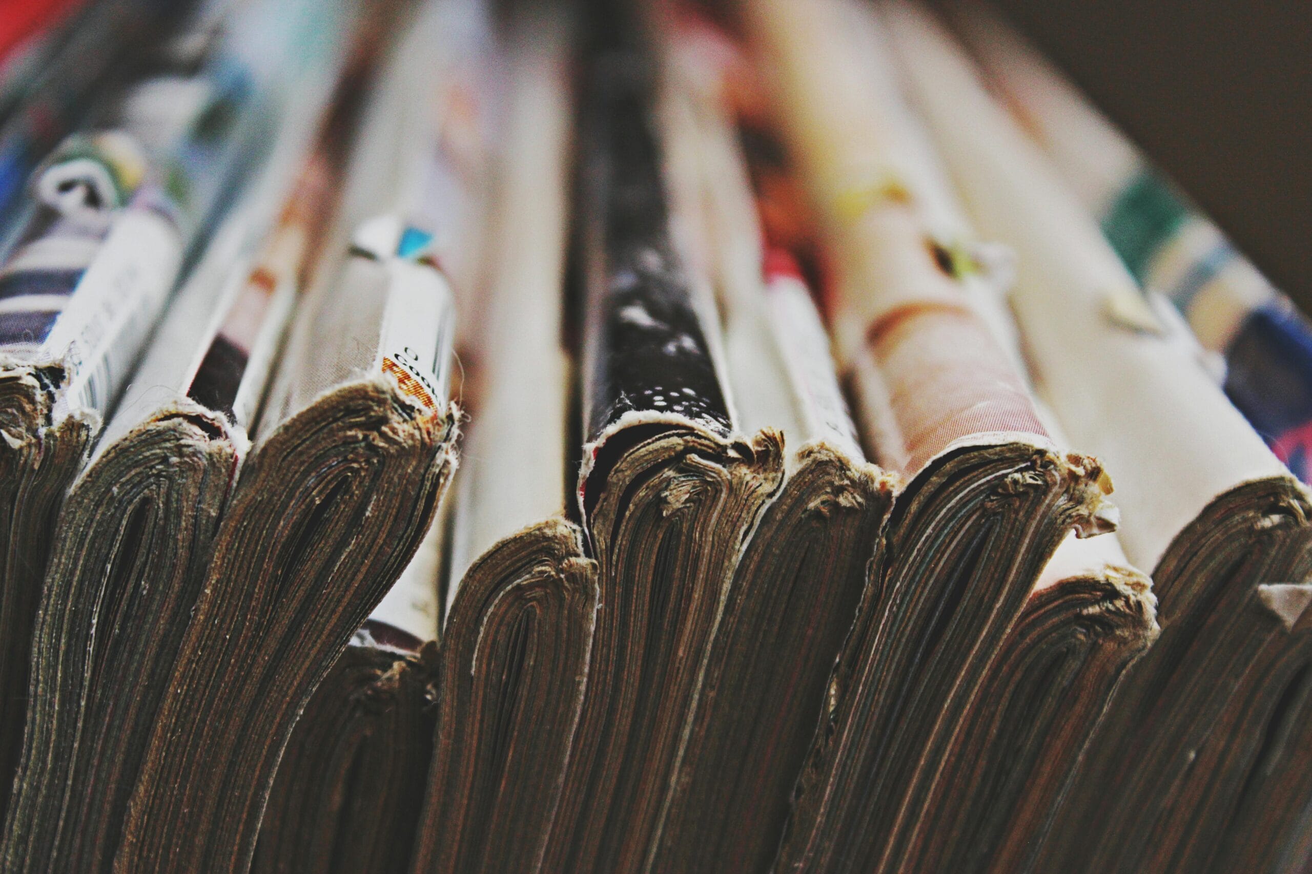 A detailed close-up image of a stack of magazines arranged in a row, showcasing their bindings.